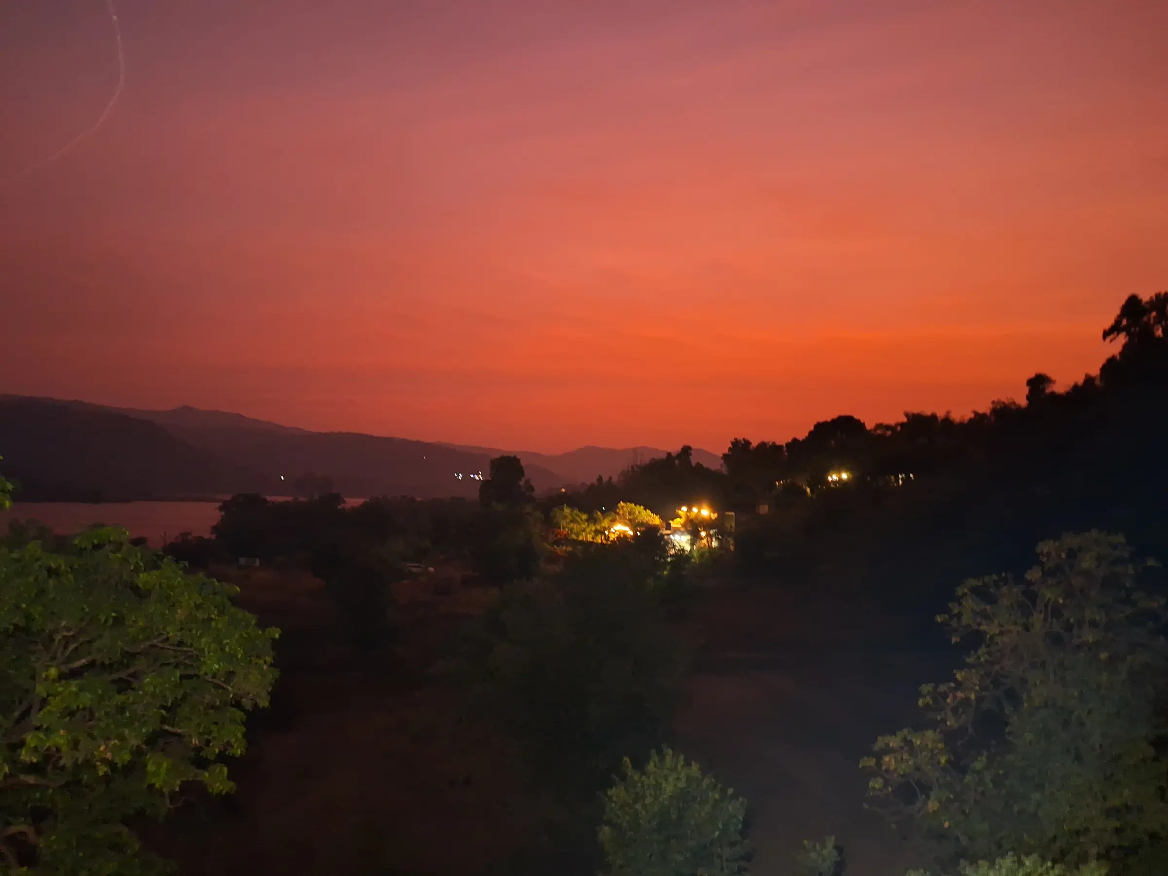 A serene sunset over a valley with glowing lights and silhouetted trees.