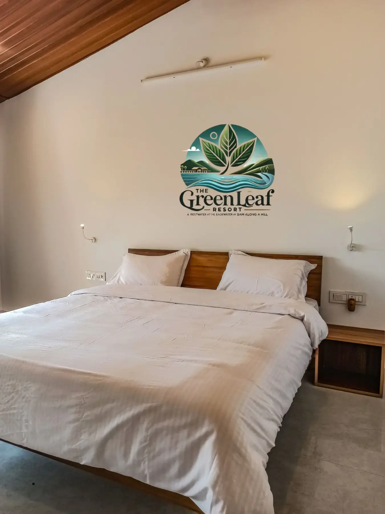 Cozy bedroom with a wooden bed and The Green Leaf Resort logo on the wall.