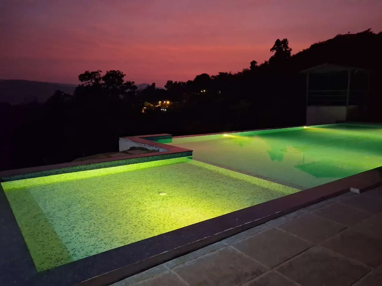 Two illuminated swimming pools at dusk with a purple sky.